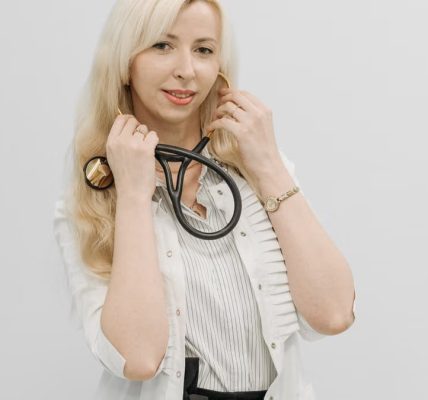 Confident female doctor posing with her stethoscope in a white coat indoors.