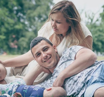 Happy family enjoying a sunny day outdoors, with parents and children lying on the grass.
